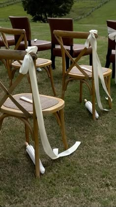 wooden chairs with bows tied to them in the grass