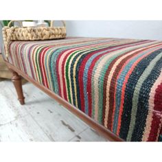 a multicolored blanket is sitting on top of a bench with a basket in the background