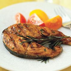 grilled salmon with rosemary garnish on a white plate next to tomatoes and oranges