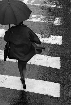 a woman walking across a street holding an umbrella over her head in black and white