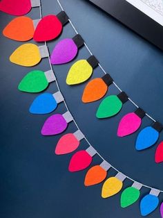 colorful paper christmas lights hanging from a string on a black table next to a computer