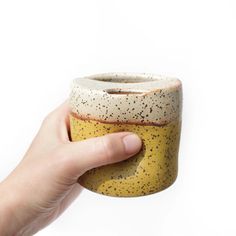 a hand is holding a yellow and black ceramic cup with speckles on it