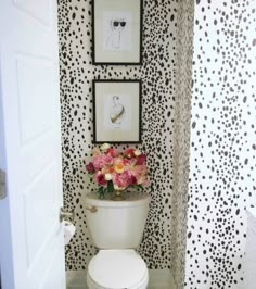 a white toilet sitting in a bathroom next to a wall with pictures and flowers on it