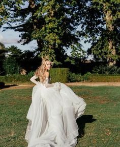 a woman in a wedding dress is walking through the grass with her back to the camera