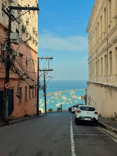 two cars parked on the side of an empty street next to some buildings with water in the background