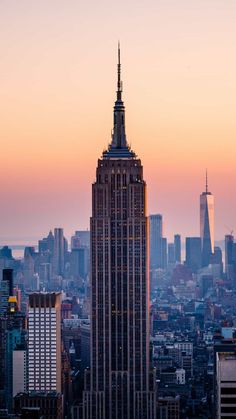 the empire building in new york city is lit up at sunset with skyscrapers behind it