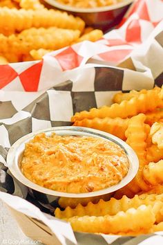 some food that is sitting on top of checkered table cloth and in bowls with dipping sauce