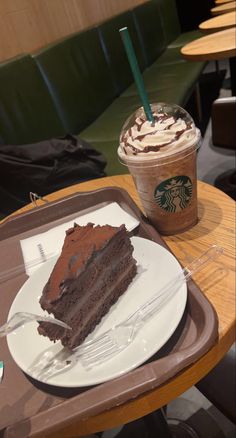 a slice of chocolate cake on a plate next to a cup of starbucks coffee with a straw in it