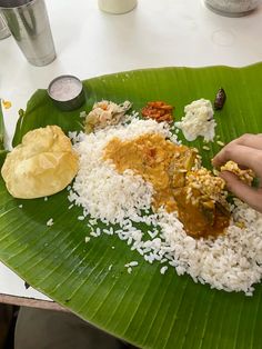 a plate with rice, meat and sauces on it sitting on a banana leaf