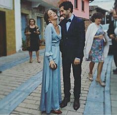 a man and woman standing next to each other on a sidewalk in front of buildings