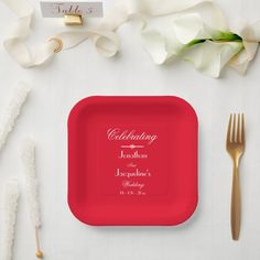 a red plate with the names of two people on it next to silverware and flowers