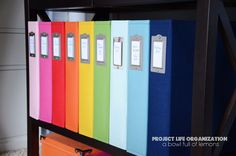 colorful file folders with labels on them in front of a black bookcase filled with books