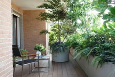 a balcony with potted plants and chairs on the outside patio, next to a brick wall