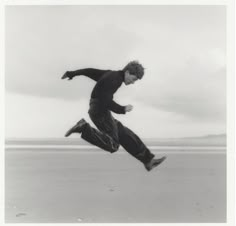 black and white photograph of a man jumping in the air with his legs spread out