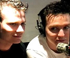 two men with headphones on and one is holding a microphone