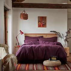 a bed with purple sheets and pillows in a bedroom next to a rug on the floor