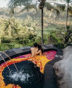 a woman sitting on the edge of a hot tub with flowers all over it and palm trees in the background