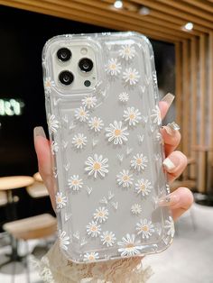 a woman holding up her phone case with daisies on it