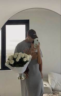 a man taking a selfie in front of a mirror holding a bouquet of white roses