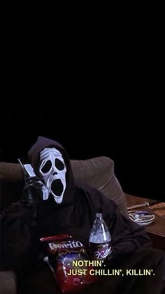 a person in a black mask sitting on a couch with a bottle and some snacks