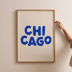 a person holding up a framed poster with the word chicago in blue ink on it