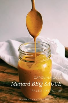 a spoon full of mustard being drizzled into a jar with the words mustard bq sauce on it