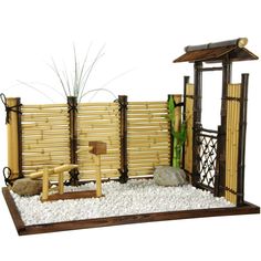 a model of a bamboo fence with rocks and gravel in the foreground, along with a small wooden bench