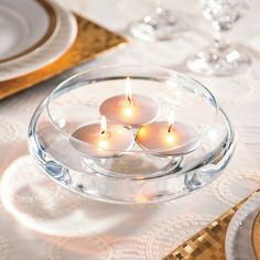 four lit candles in a glass bowl on a table