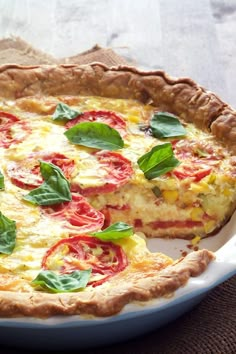 a quiche with tomatoes, cheese and basil leaves on the top is ready to be eaten