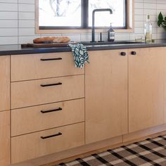 a kitchen with wooden cabinets and black counter tops next to a window that has a checkered rug on the floor