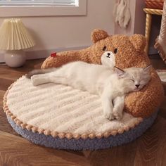 a white cat laying on top of a teddy bear bed next to a stuffed animal