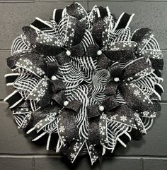 a black and white wreath hanging on the wall next to a gray brick wall with snowflakes