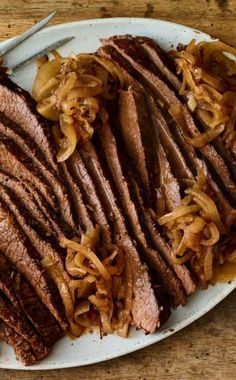 sliced meat and onions on a white plate with a knife next to it, sitting on a wooden table