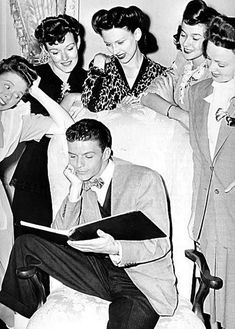 black and white photograph of four people sitting on a bed looking at something in front of them