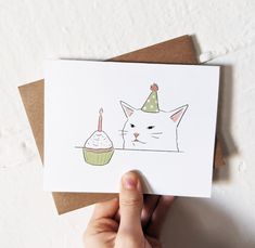 a hand holding up a card with a cat and cupcake on it