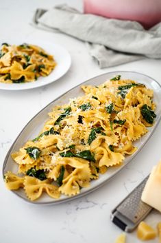 pasta with spinach and parmesan cheese is on a plate next to a butter knife