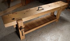 a wooden bench sitting on top of a floor next to a shelf filled with tools