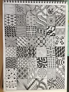 an open notebook with black and white doodled designs on it, sitting on top of a desk