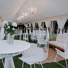 white chairs and tables are set up under a tent for an outdoor wedding reception with flowers in a vase