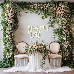 a table with two chairs and a sign that says mr and mrs on it, surrounded by greenery