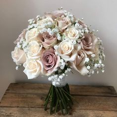 a bouquet of white and pink roses in a glass vase on a wooden table with baby's breath