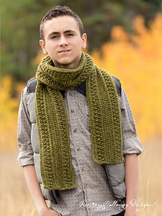 a young man wearing a green knitted scarf in the middle of a grassy field