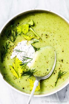 a white bowl filled with broccoli soup topped with sour cream and sprigs