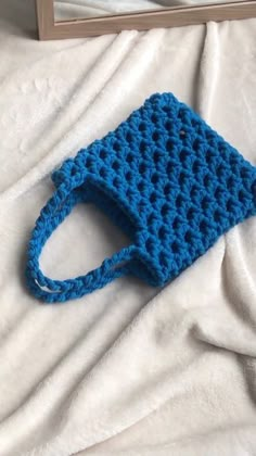 a blue crocheted bag sitting on top of a white bed next to a mirror