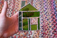 a hand holding up a small green house shaped glass ornament in front of a rug