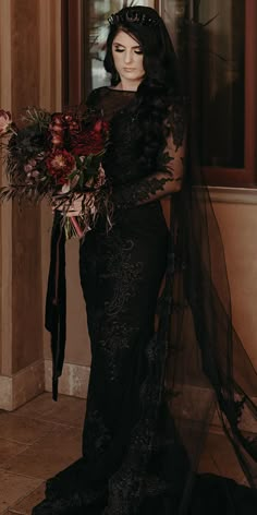 a woman in a black dress is holding a bouquet and posing for the camera with her long veil over her head