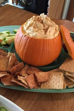 an orange pumpkin sitting on top of a green plate filled with crackers and veggies