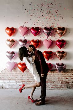 a man and woman are kissing in front of hearts on the wall with confetti