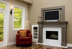 a living room with a red chair and television on the fireplace mantel in front of two windows