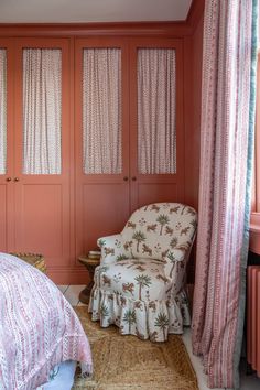 a bedroom with pink walls and curtains on the windowsills, a chair in front of a bed